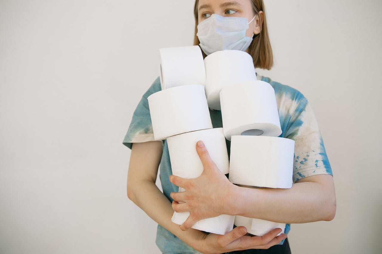 gallery-01 Woman wearing a face mask holding several toilet paper rolls indoors.